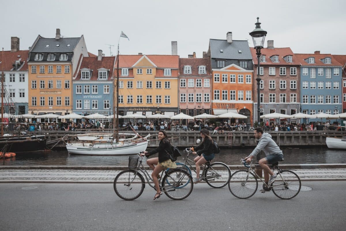 Na foto 3 pessoas andando de bicicleta pelos canais de Nyvan em Copenhague