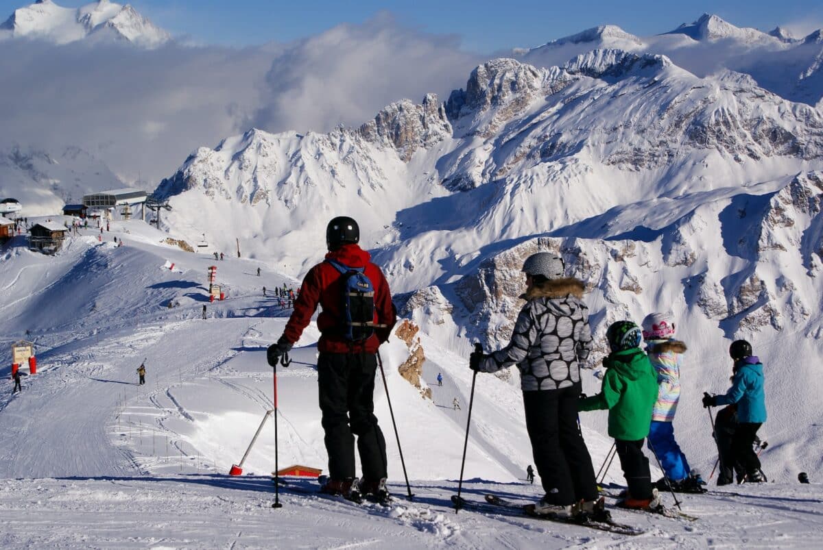 Foto de 3 pessoas de esqui olhando para uma montanha com gelo, numa estação de esqui