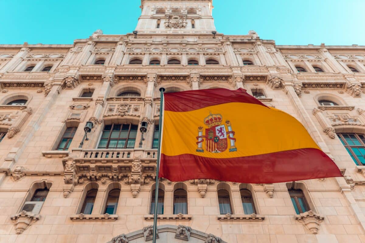 Bandeira da Espanha em frente ao um monumento, nas cores amarelo e vermelho