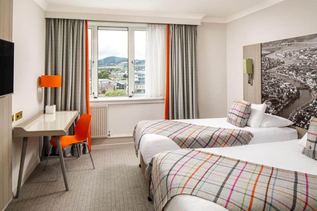 quarto do hotel mercure inverness - duas camas de solteiro em tons de laranja com vista para a cidade