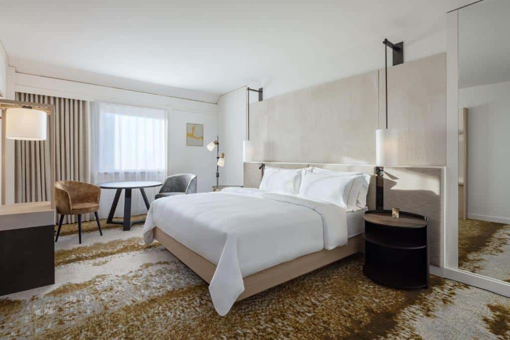 Quarto do The Westin Grand Frankfurt - cama de casal branca e quarto bem arejado e claro em tons brancos e bege.