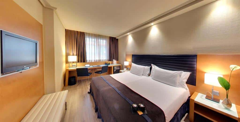 quarto do Hotel Silken Indautxu em bilbao - cama de casal com roupa de cama branca e marrom, quarto em tons alaranjados e bem iluminado