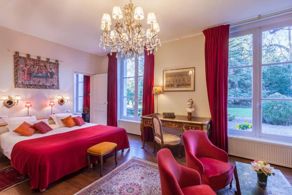 Quarto do Hotel Le Clos d'Amboise - cama de casal grande, em tons branco e vermelho com duas janelas grandes com mesa de trabalho e duas poltronas.