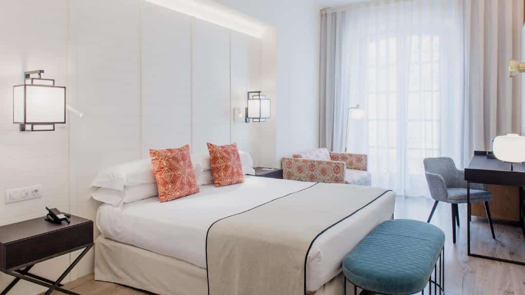 Hotel Molina Lario em Málaga. Quarto de casal claro, todo branco com almofadas em tons vermelhos e mesinha com poltrona.