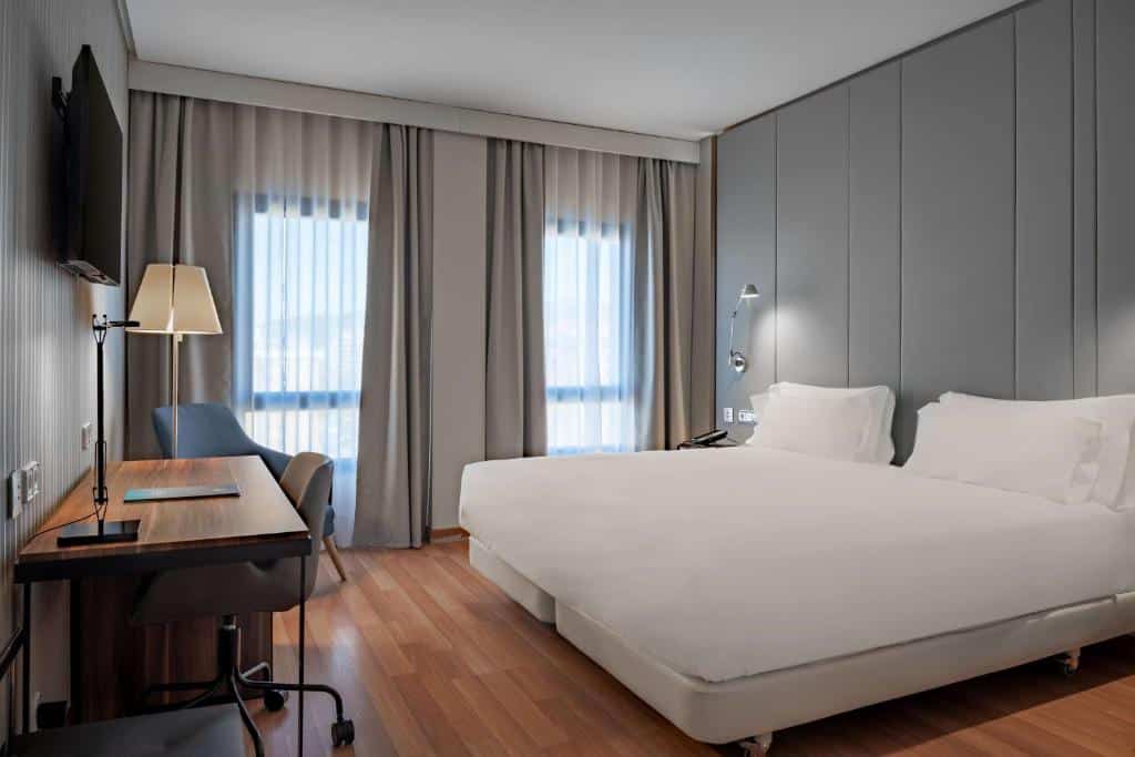 NH Ciudad de Cuenca - quarto com cama de casal em tons de branco e cinza. Com escrivaninha e televisão e dois janeloes