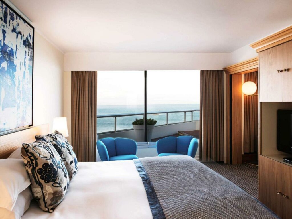 Quarto do Sofitel Biarritz Le Miramar Thalassa  - quarto com vista para o mar em tons de marrom, branco e azul. cama de casal com almofadas azuis
