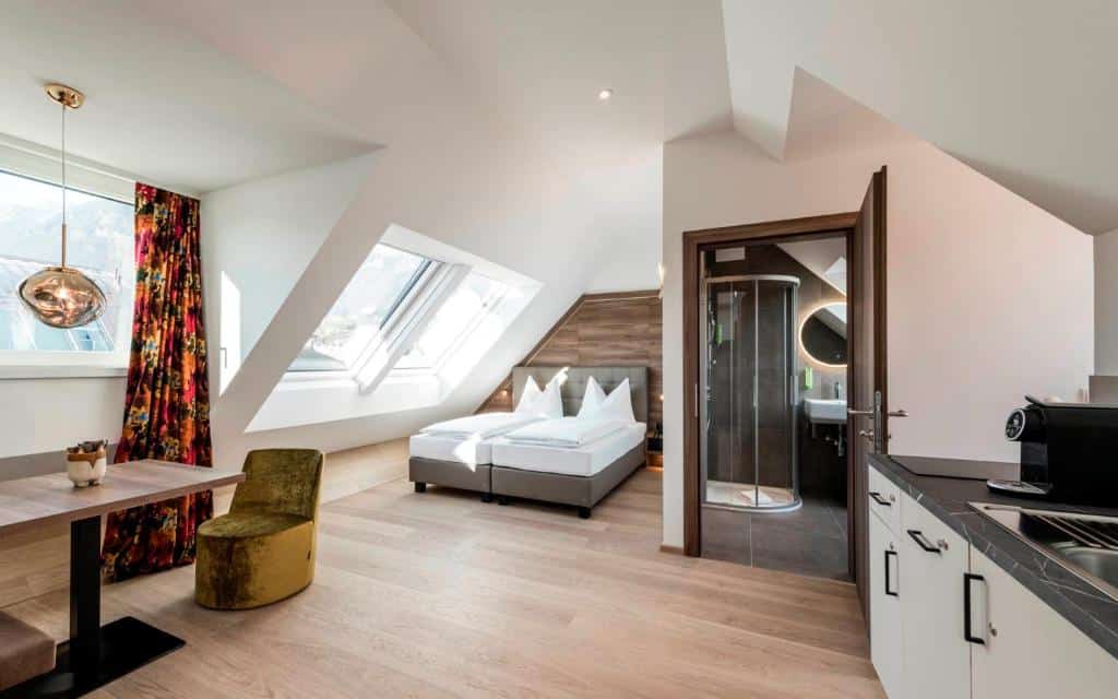 Hotel Zach em Innsbruck- quarto em tons de branco , cama de casal com cortina em tons vermelhos e mesa com cadeira