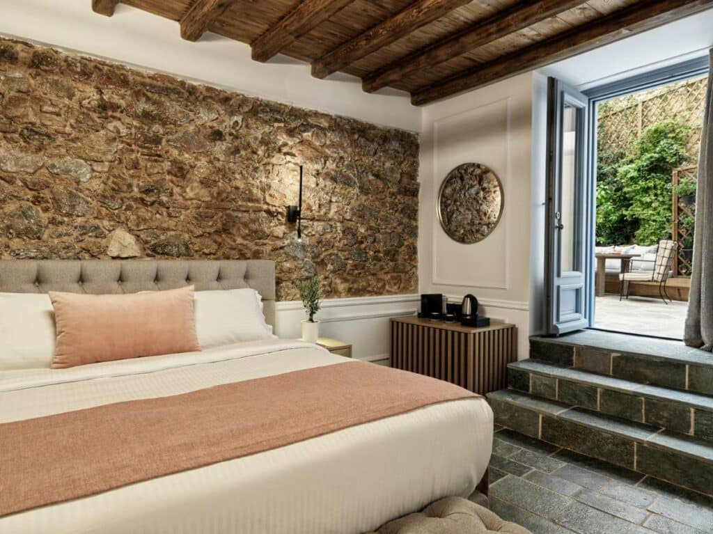Quarto do hotel A77 Suites by Andronis em Atenas - cama do tipo king com roupa de cama claras e parede de pedra com sacada