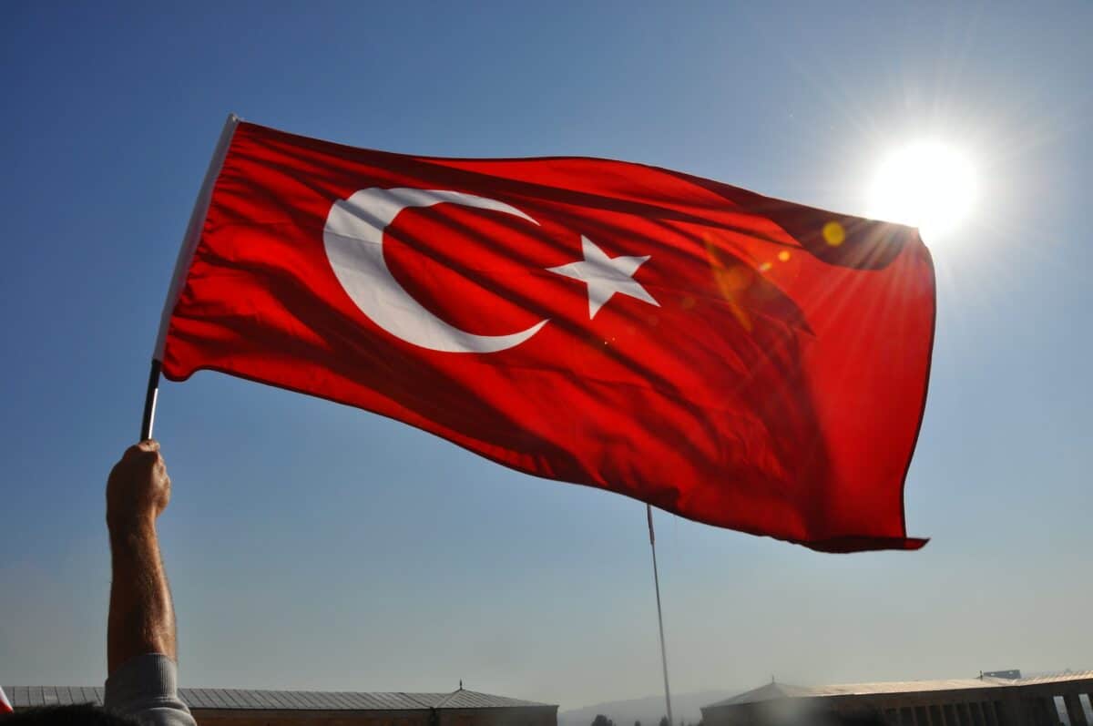 Bandeira da Turquia - vermelha com uma lua e estrela, com uma pessoa segurando mostrando apenas o braço e ao fundo céu azul