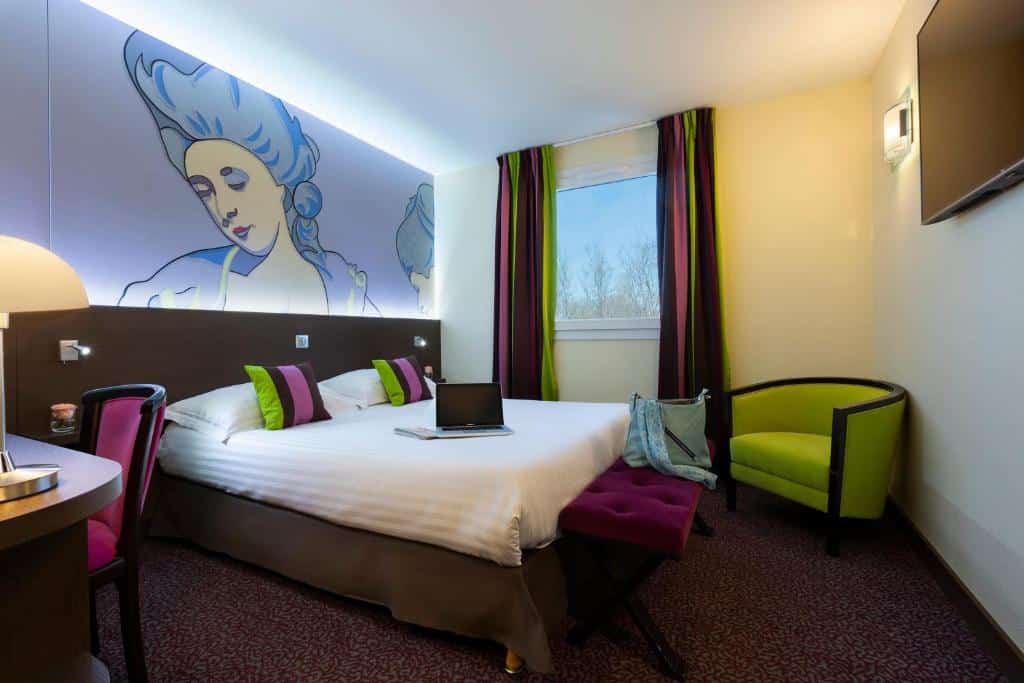 Quarto do B&B HOTEL Colmar Liberté 4 étoiles cama de casal com almofadas e cortinas em verde e rosa, quadro. de mulher em tom de azul.