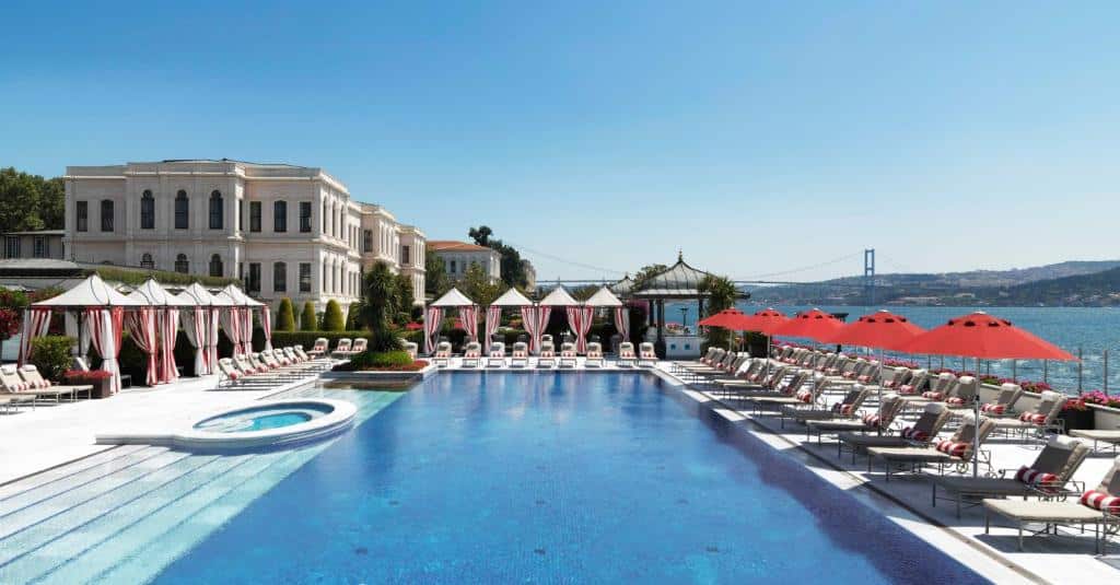 Vista externa do Four Seasons Hotel Istanbul na Turquia. Ao lado do estreito de bosforo com piscina, espreguiçadeiras com guarda sois vermelho e construção no estilo romano