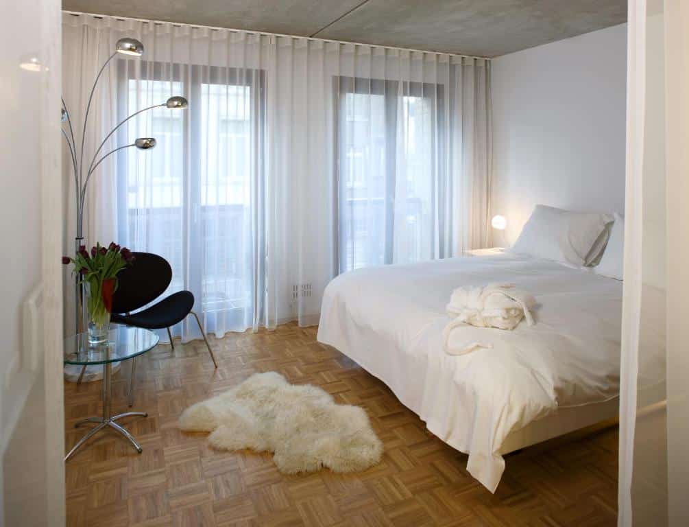 Quarto do hotel bank na Antuérpia, quarto todo branco, com cama de casal, tapete de pelos e cadeira preta.