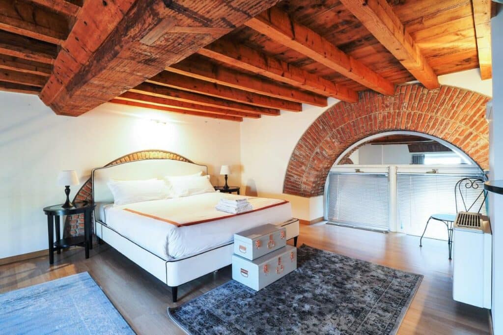 Unique Duomo Luxury Property  - quarto do apartamento. Cama de casal com roupa de cama clara e paredes brancas com tijolos a mostra. Decoração luxo