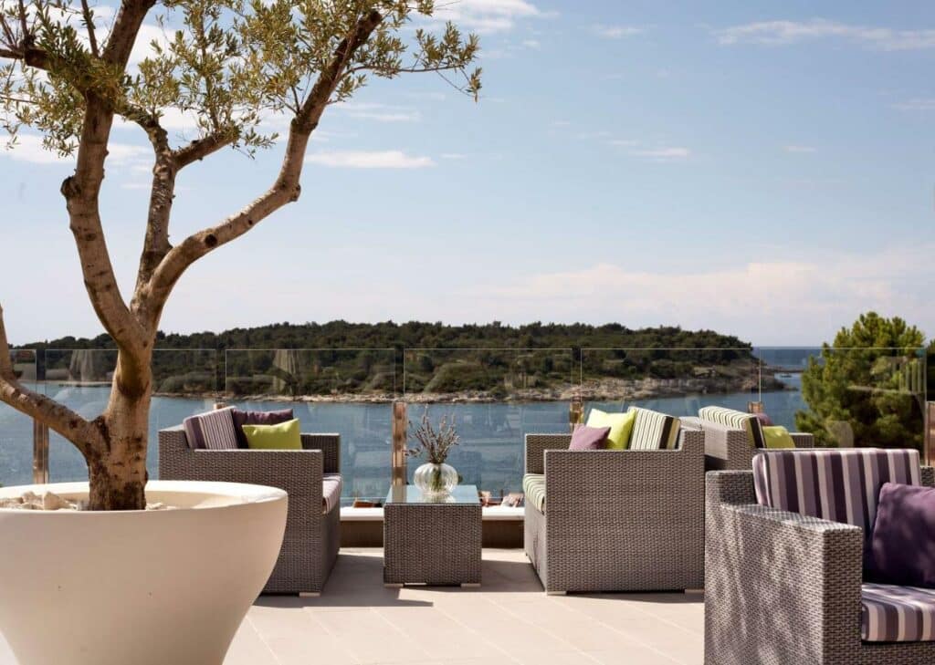 Terraço com vista para o mar, com poltronas e sofás, mesa de centro, um lindo vaso com arvore, esta imagem representa um dos ambientes do Hotel Park Plaza Histria na cidade Pula, em Istria.