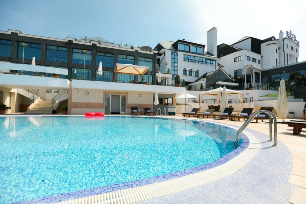 Area e fachada externa do Hotel com piscina e cadeiras de sol, essa imagem representa um dos ambientes do Hotel Villa Breg em Bosnia e Herzegovina.