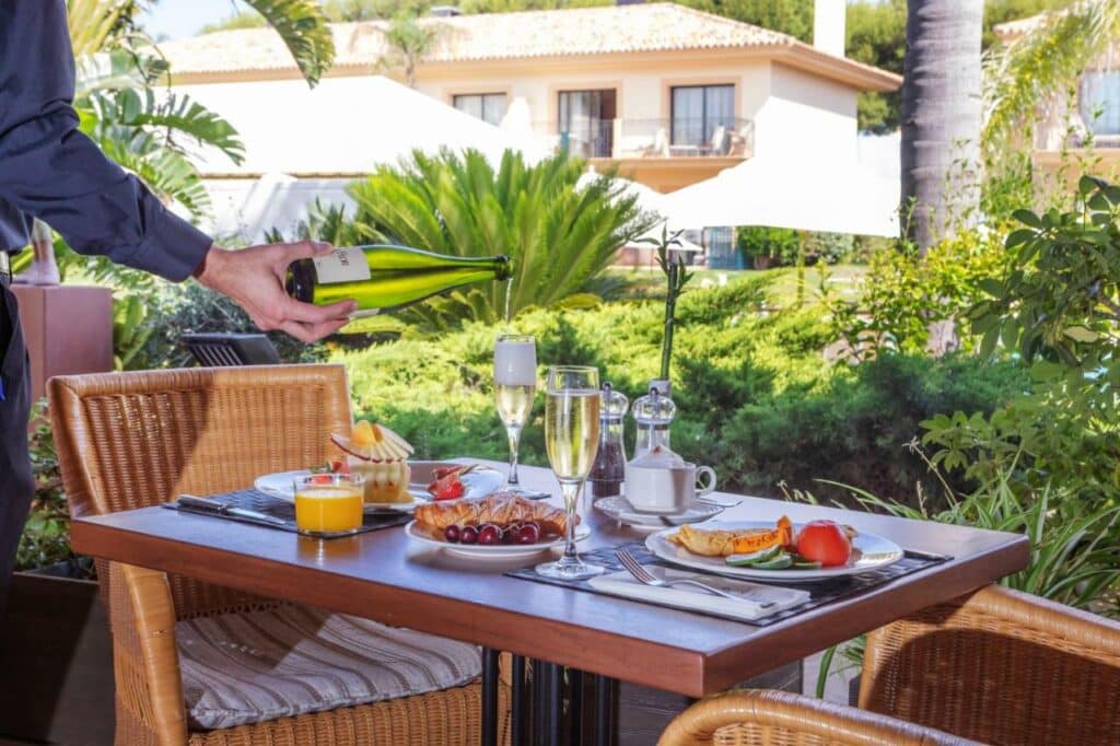 linda mesa de café no jardim, posta com frutas, champagne, croissants, suco, representa um dos ambientes do hotel La quinta Menorca by PortBlue Boutique.