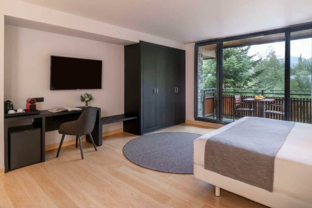 NH Collection Andorra Palomé - quarto com cama de casal, armários pretos mesinha de apoio com cafeteira, sacada com móveis e vista para floresta.