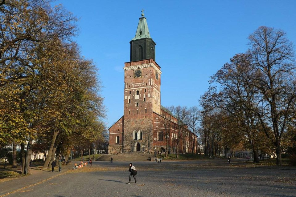 Igreja Catedral de Torku com uma torre central que detaca-se pela altura, com um crucifixo na extremidade superior. Há algumas janelas na torre, e uma porta central. Há algumas árvores no entorno da Catedral e algumas pessoas na foto.