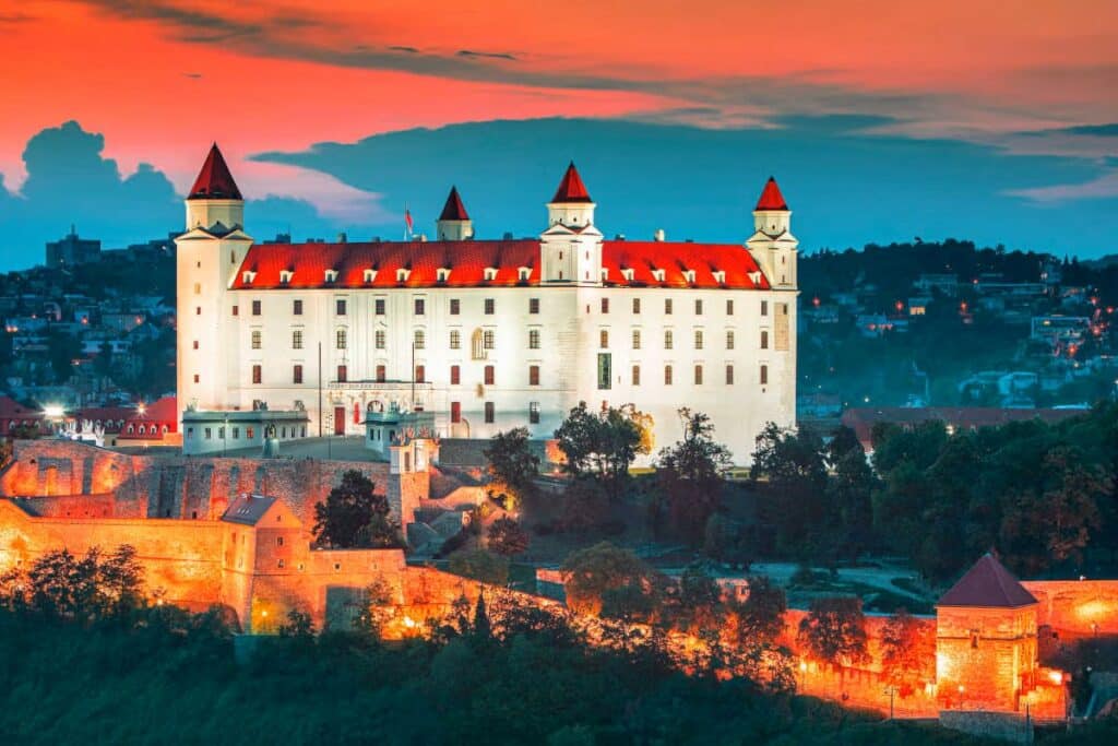 Castelo de Bratislava na Eslováquia ao fundo da imagem. No entorno é possível observar construções e vegetação. 