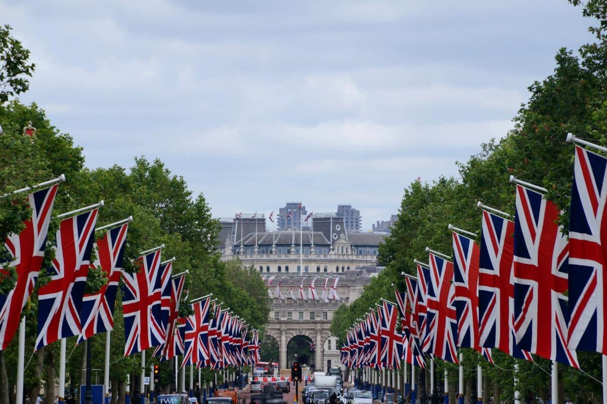 Bandeiras do Union Jack, Union Flag ou Reino Unido, em Londres, estão alinhadas em ambos os lados de uma estrada que leva a um arco distante, com árvores e edifícios ao fundo, para representar guia de viagem para o Reino Unido