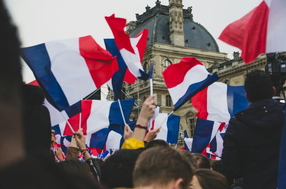 Bandeiras da França. Listrada em branco, azul e vermelho, com o Louvre ao fundo.