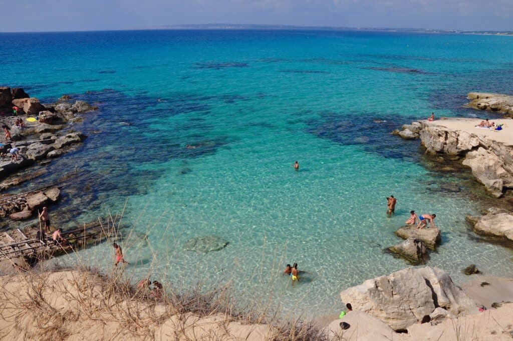 Formentera, ilha próximo a Ibiza. Mar azul claro com pedras e pessoas nadando. 