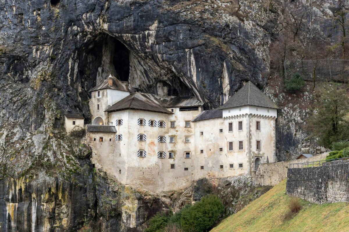 Castelo Predjama em uma encosta rochosa de uma montanha com janelas visíveis, paredes desgastadas e vegetação em primeiro plano, para representar seguro viagem para Eslováquia.