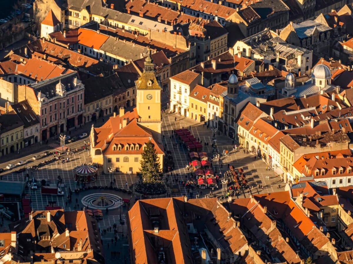 Piata Sfatului ou Praça do Conselho, em Brasov na Região da Transilvânia. - Vista aérea de uma praça da cidade com uma torre do relógio, cercada por edifícios históricos e uma árvore de Natal no centro.