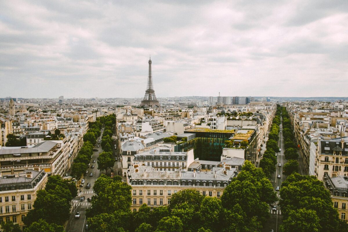 Vista aérea de Paris, na França, com a Torre Eiffel ao longe, cercada por fileiras de árvores e edifícios sob um céu nublado, representando eSIM para França.