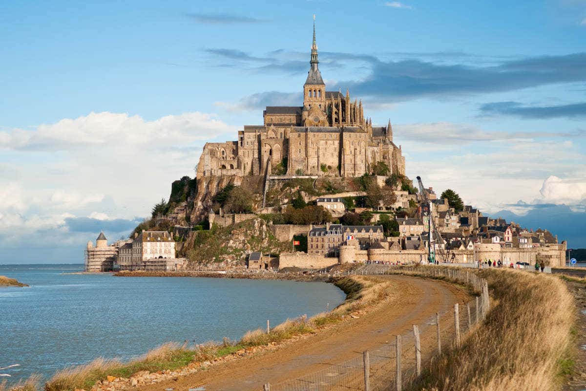 O Monte Saint-Michel, uma abadia e vila histórica, fica em uma ilha rochosa conectada por uma ponte, cercada por água.