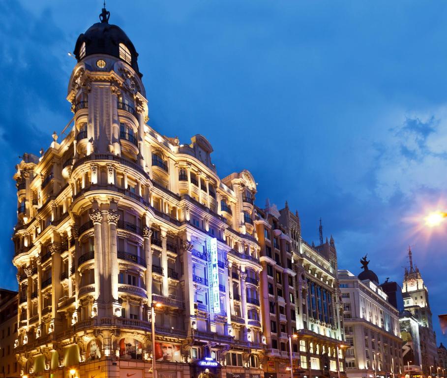 Edifício histórico do hotel Atlántico, Espanha, ornamentado iluminado ao anoitecer em uma rua movimentada da capital da Espanha, com um céu azul nublado sobre a cabeça, para representar hotéis em Madri.