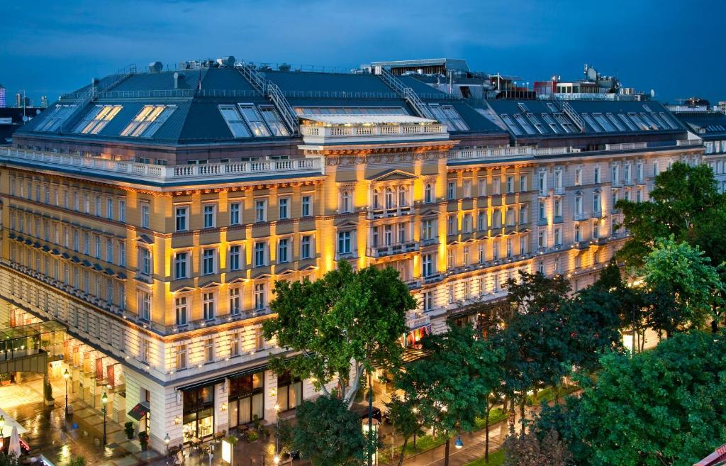 Fachada do Grand Hotel Wien em Viena, na Áustria, um prédio grande e histórico com arquitetura ornamentada e iluminação aconchegante, cercado por árvores e ruas da cidade ao anoitecer.