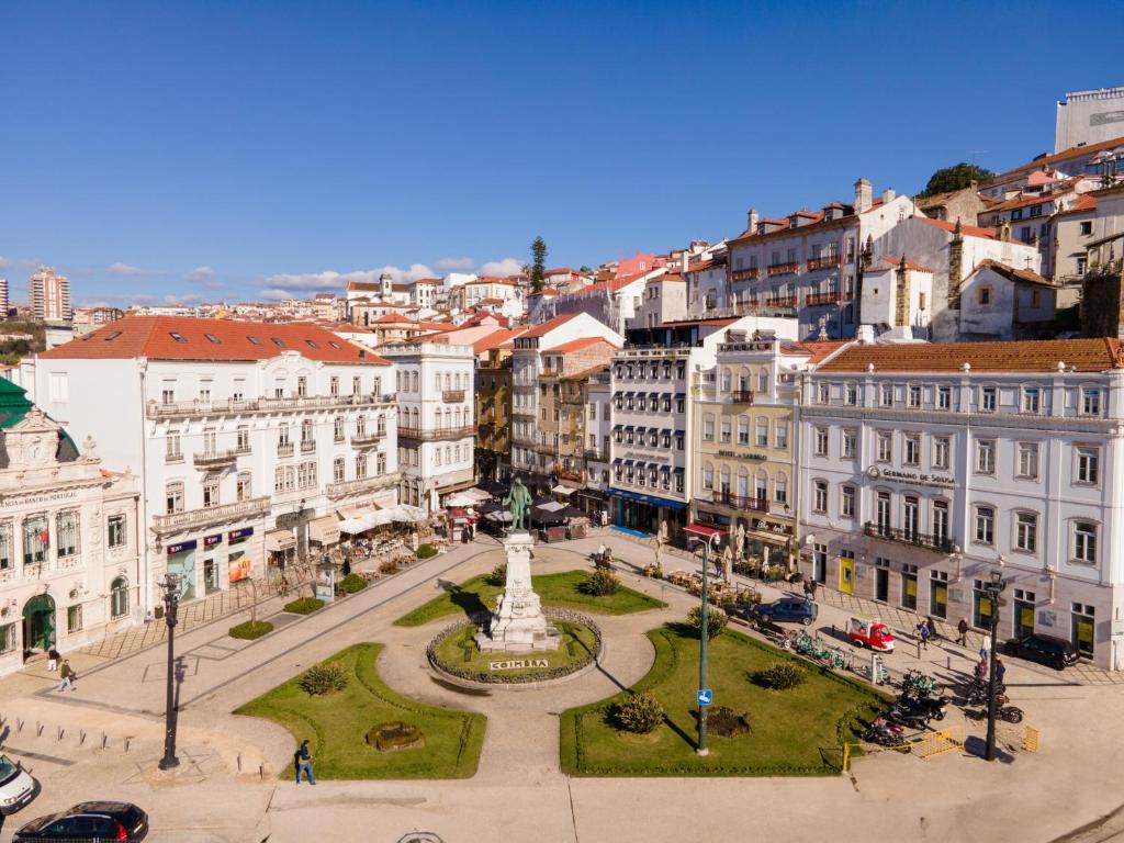 Uma praça da cidade de Coimbra, com uma estátua central, cercada por edifícios históricos sob um céu azul claro, para representar hotéis em Coimbra.