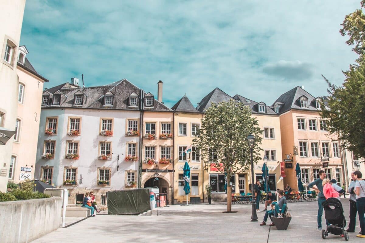 Uma praça pública no bairro Grund, centro de cidade de Luxemburgo, com prédios históricos, árvores e pessoas andando, para representar guia para Luxemburgo.